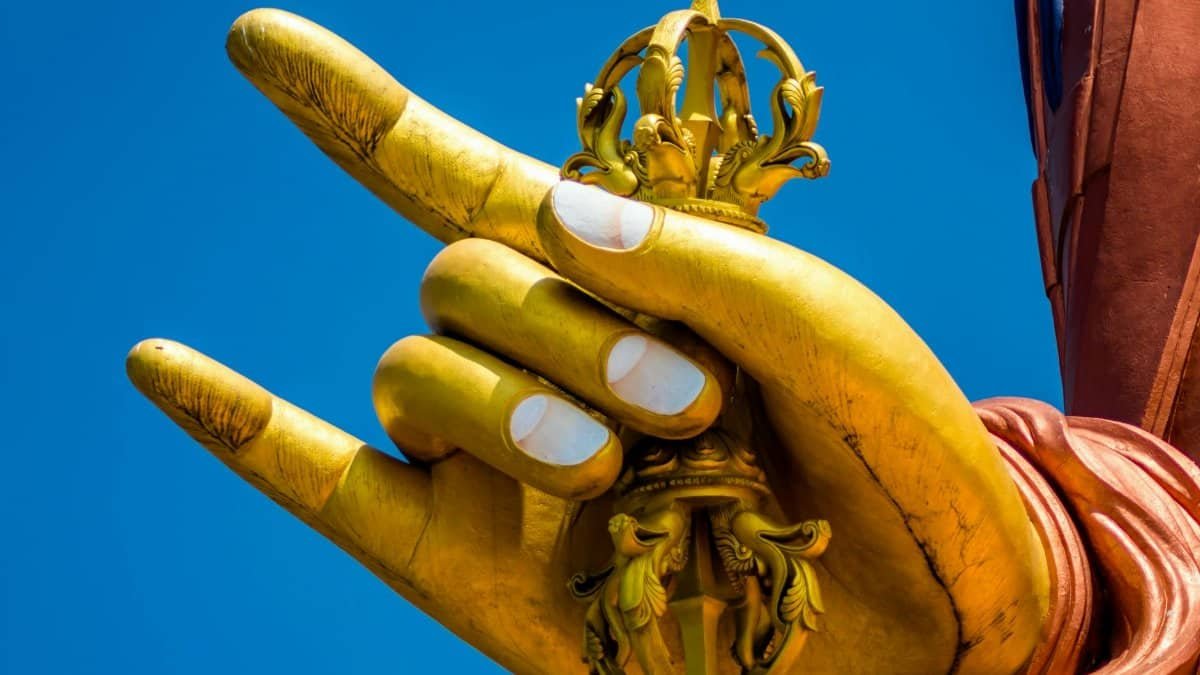 Close-up of a golden Buddha hand statue holding a traditional symbol in South Sikkim, India.