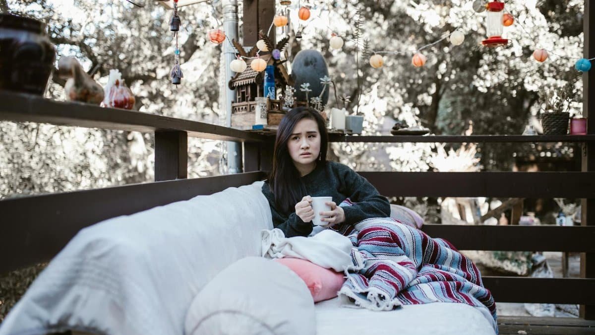 Woman enjoying a quiet afternoon with tea on a patio, wrapped in a colorful blanket.