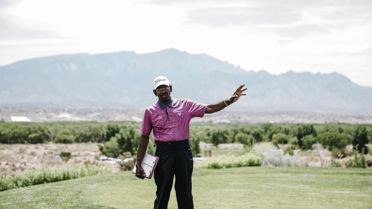A golf caddie gestures on a scenic golf course with mountains in the background, exuding leisure and relaxation.
