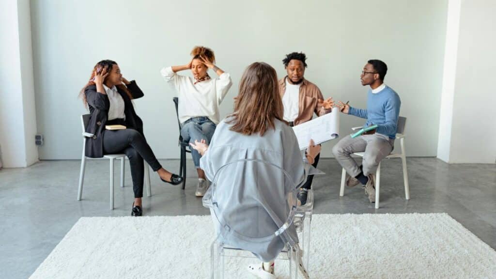 People engaging in a group therapy session indoors, discussing mental health topics.