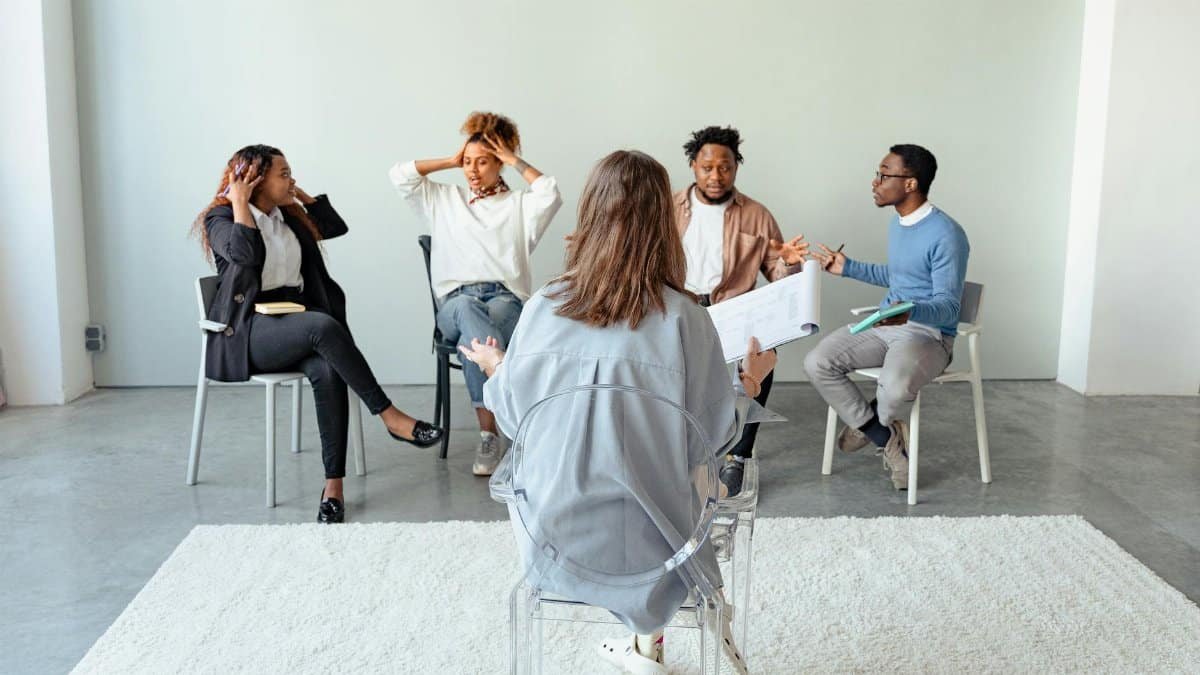 People engaging in a group therapy session indoors, discussing mental health topics.
