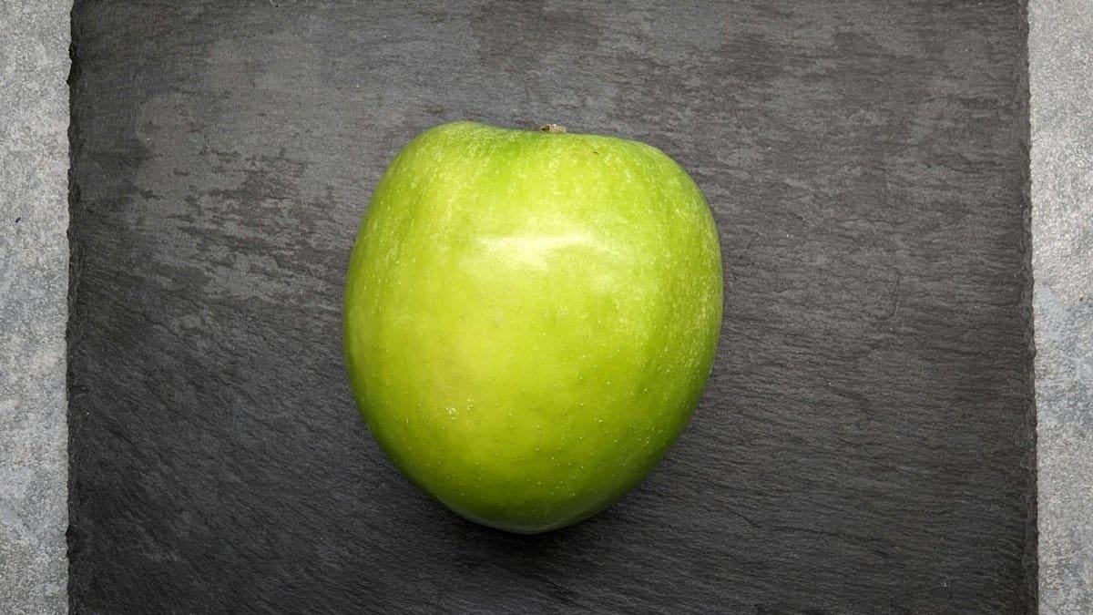 A vivid green apple placed on a textured dark slate, showcasing minimalist food photography.