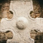 Close-up of a Celtic stone cross within ancient stone walls, exuding historical charm.