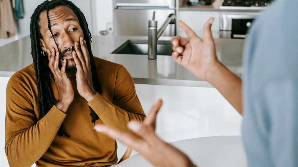 Young African American male sitting at table with hands on face and having conflict with female on kitchen