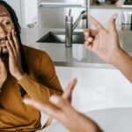 Young African American male sitting at table with hands on face and having conflict with female on kitchen