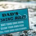 A close-up of a fun sign highlighting dad's fishing rules placed by a river, perfect for Father's Day.