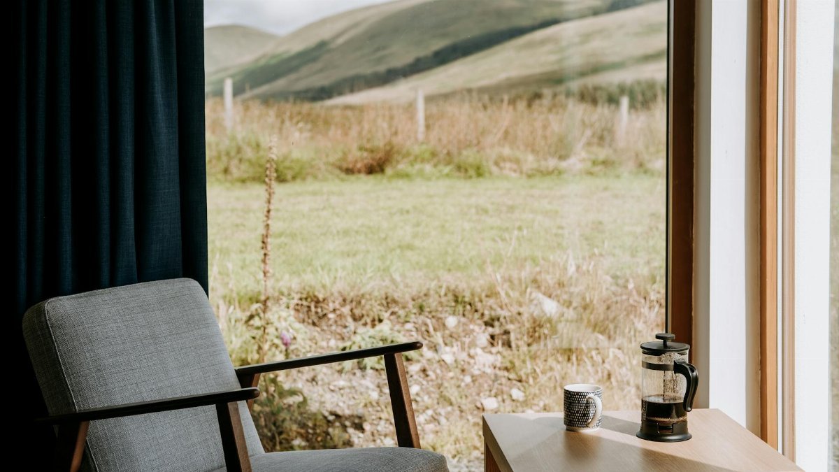 Cozy armchair against table with French press with espresso and mug against glass wall at home
