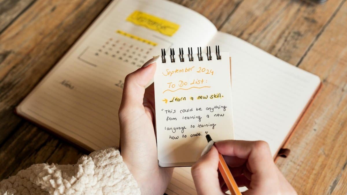 A person writes a September 2024 to-do list in a notebook, focusing on learning new skills.