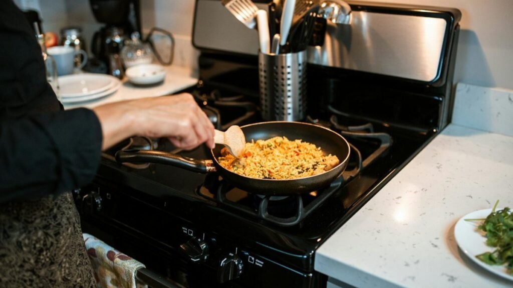 A person cooking rice pilaf using a frying pan on a gas stove in a home kitchen.