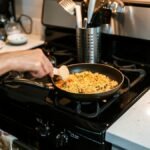 A person cooking rice pilaf using a frying pan on a gas stove in a home kitchen.