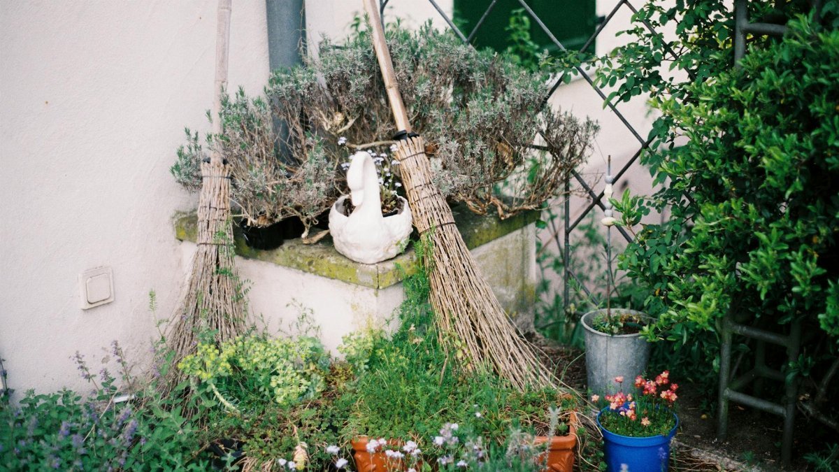 Charming garden corner featuring rustic brooms, potted plants, and a decorative swan.