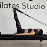 Woman exercising on a Pilates reformer in a modern studio setting, promoting fitness and flexibility.