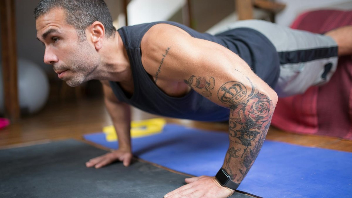 Adult man performing push-ups on a yoga mat, showcasing tattoos and fitness lifestyle.