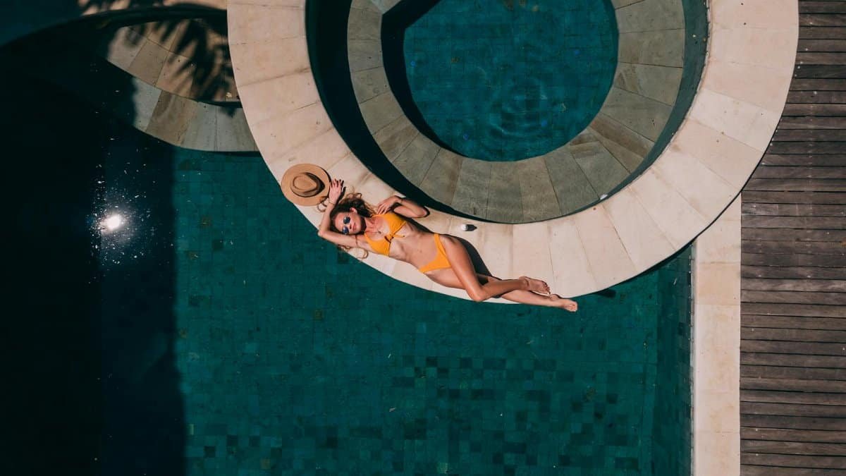 Woman sunbathing on a round pool edge in swimwear. Aerial view on a sunny day.