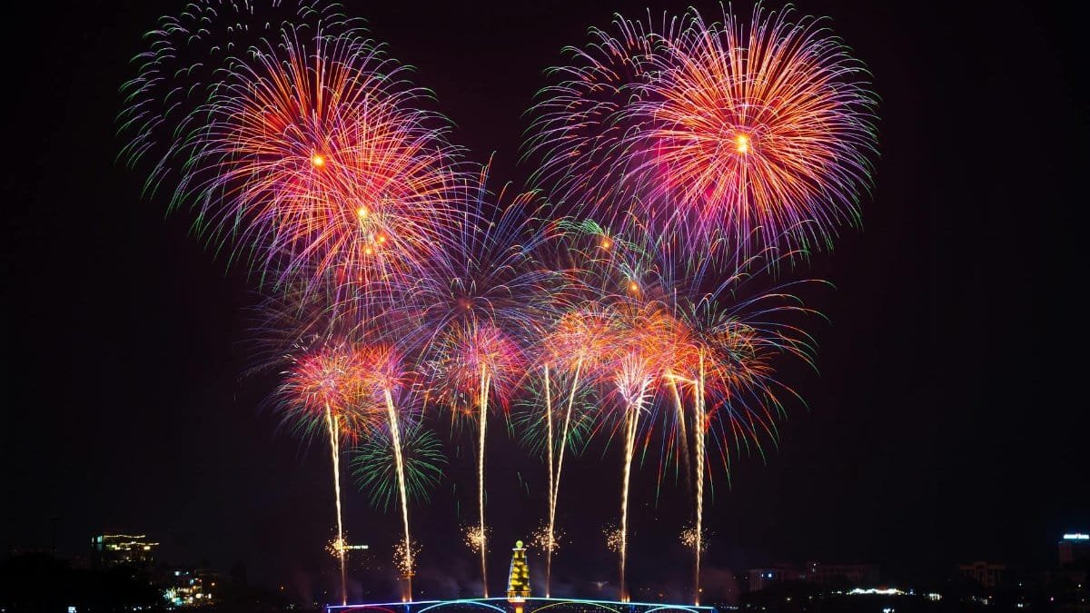 Vivid fireworks burst over a peaceful water scene, lighting up the night sky with colorful reflections.