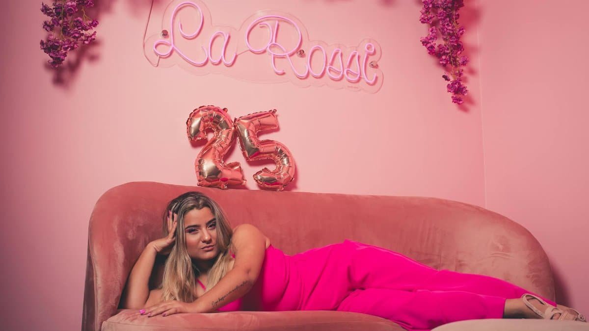 Elegant woman in pink outfit on sofa with '25' balloons, perfect for birthday celebration themes.