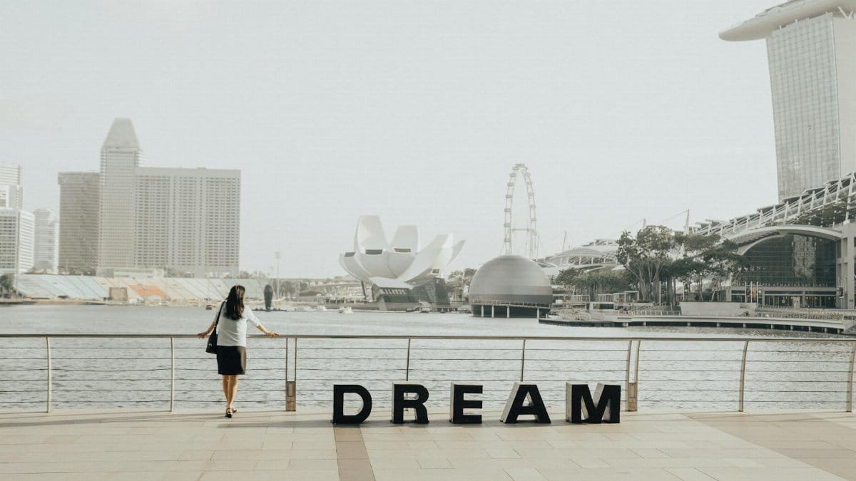 A woman gazing at the iconic Marina Bay Sands skyline in Singapore with 'Dream' letters foregrounded.