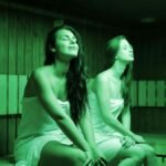 Two women in a sauna, wrapped in towels, enjoying relaxation and warmth indoors.