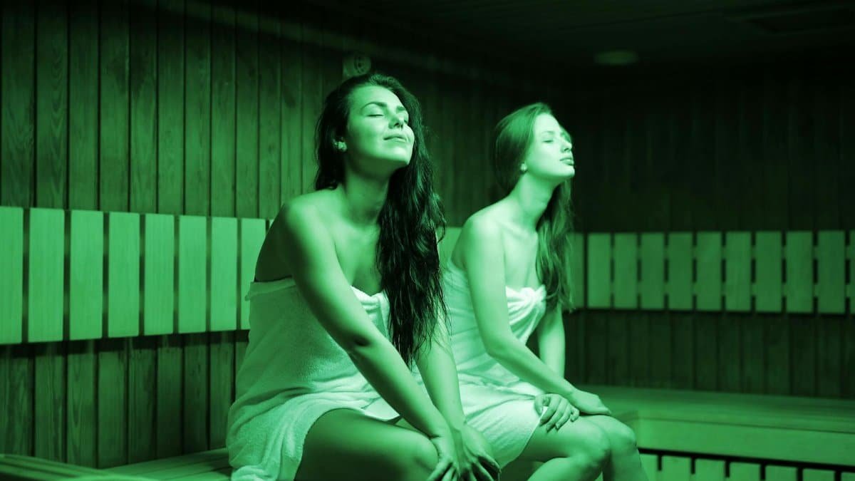Two women in a sauna, wrapped in towels, enjoying relaxation and warmth indoors.