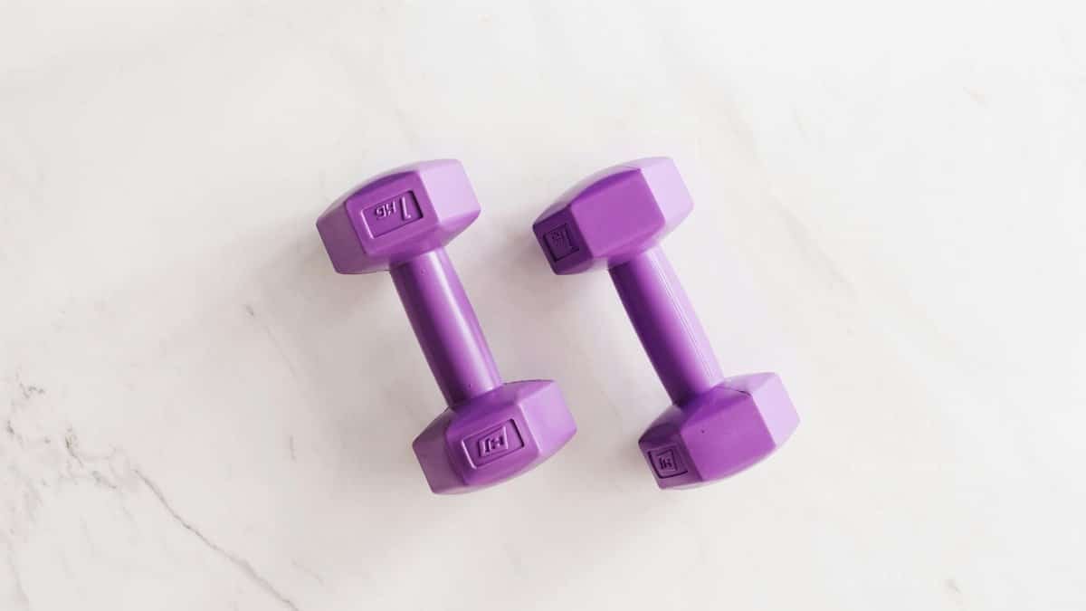 Overhead shot of two purple dumbbells on a white marble surface.