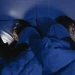 A couple lying in bed using smartphones at night, illuminated by screen light.