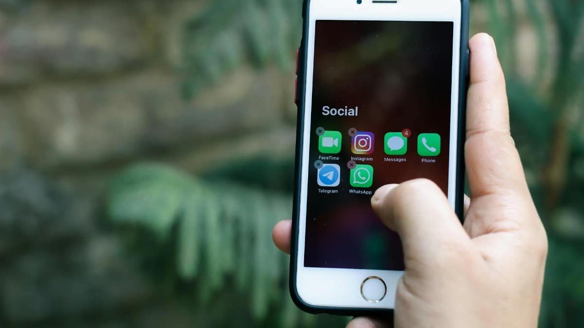 Close-up of a hand holding a smartphone displaying social media apps outdoors.