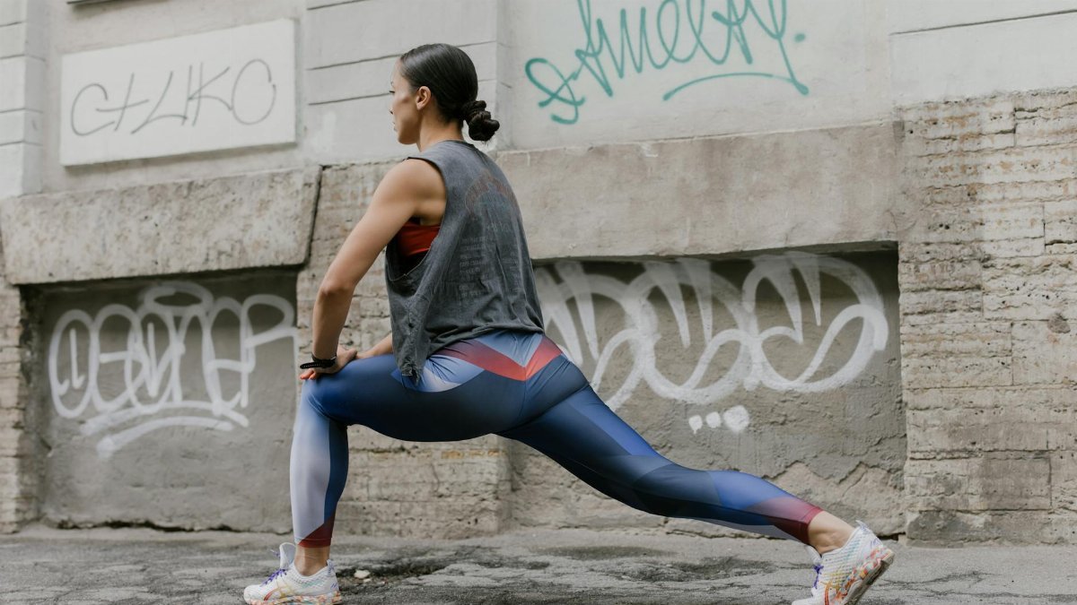 Woman doing lunges for fitness against an urban graffiti wall, showcasing exercise and wellness.