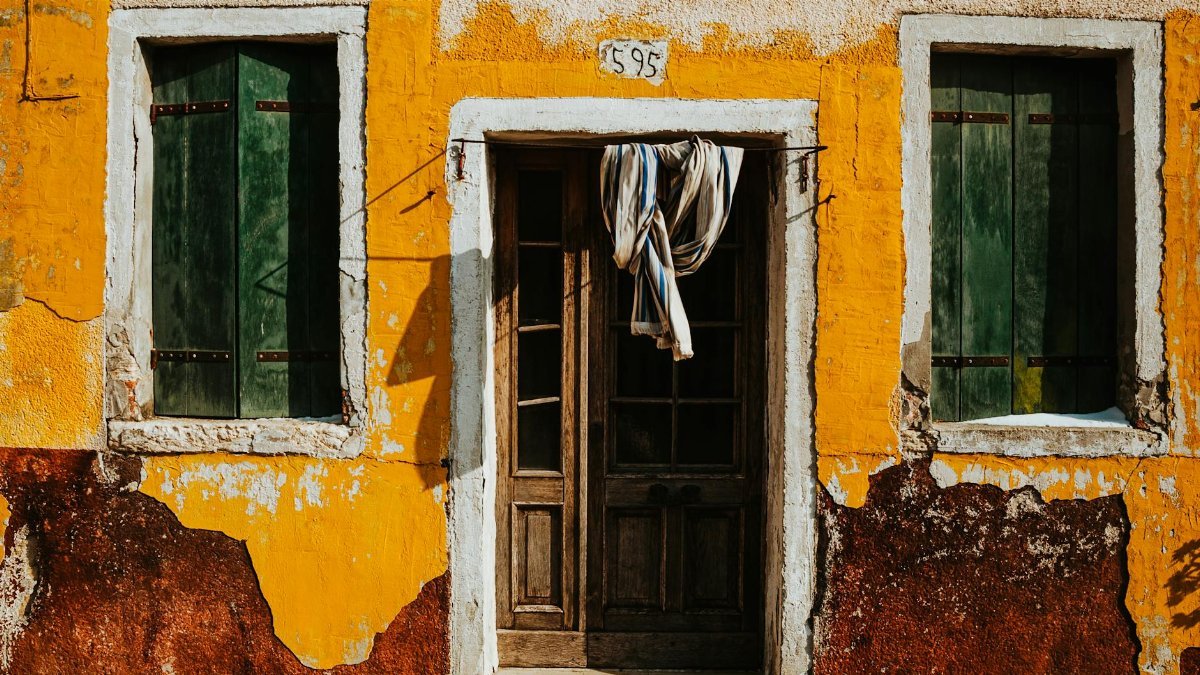 A vibrant, rustic exterior of a building in Venice with orange walls and green shutters.
