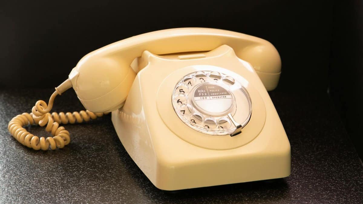 Classic beige rotary dial telephone on dark surface, evoking nostalgia and retro style.