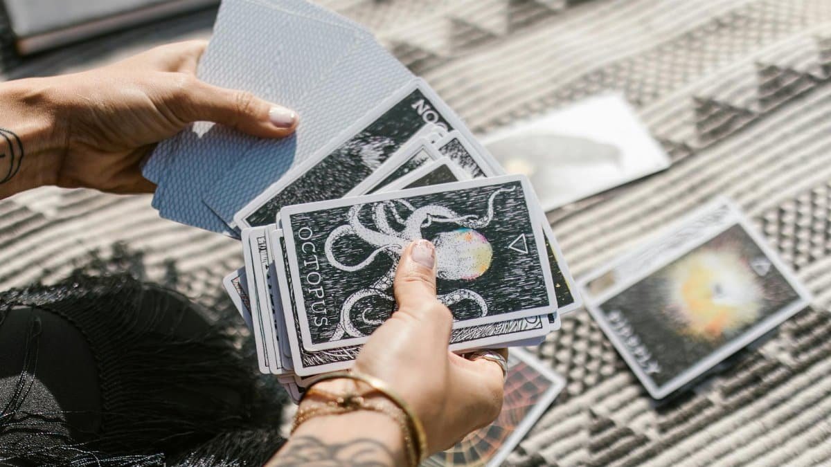 Hands holding tarot cards during a reading session on a patterned mat.