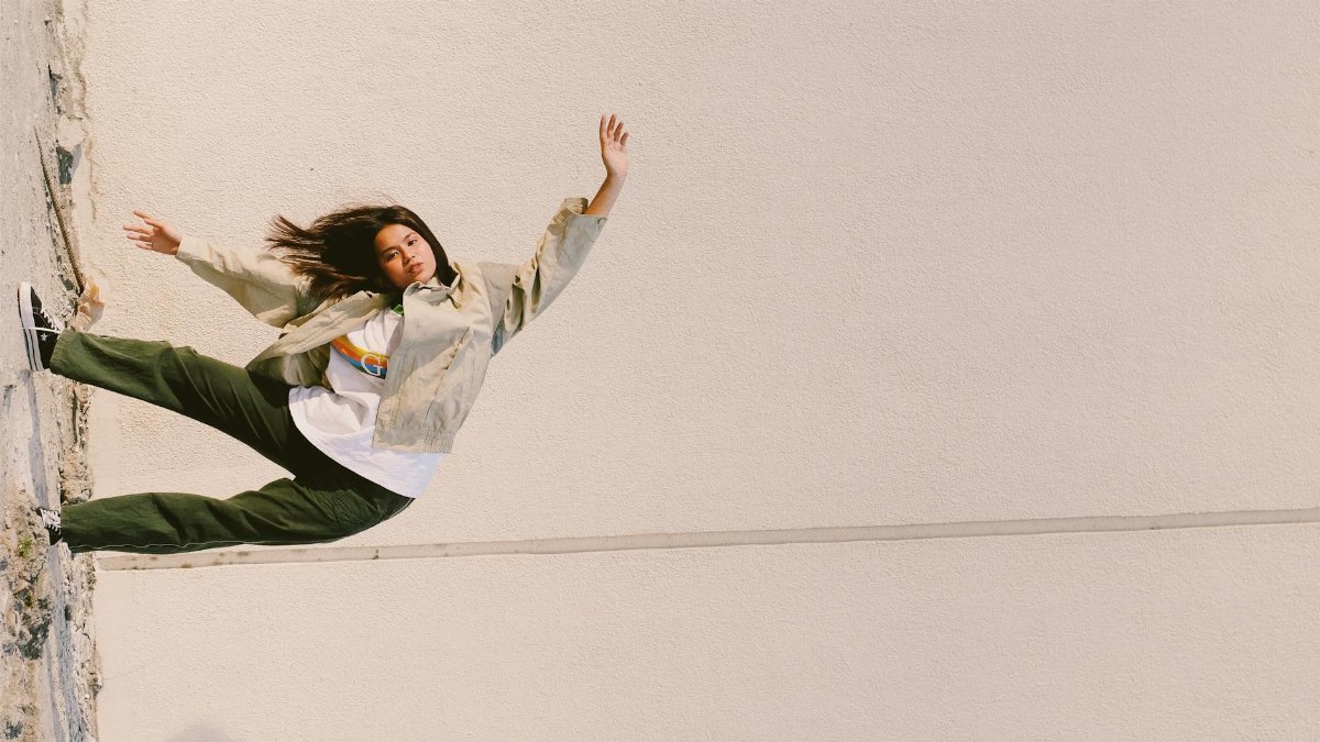 Fashion model leaning creatively against a plain wall outdoors during the day.