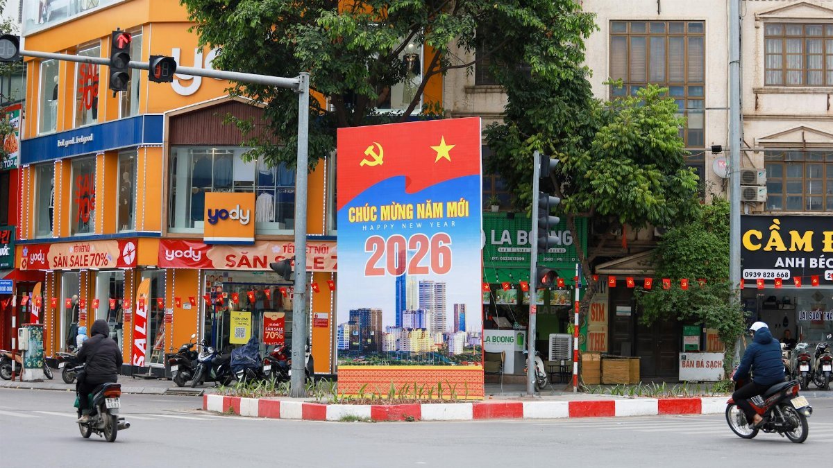 Vibrant Hà Nội street scene featuring a New Year 2026 billboard, motorcycles, and colorful shops.