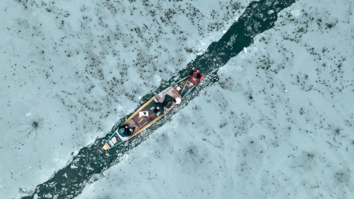 Aerial view of kayakers breaking through a frozen lake in winter.