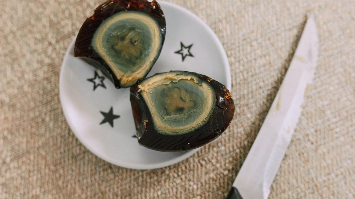 Detailed view of a sliced century egg on a decorative plate with a knife on burlap.