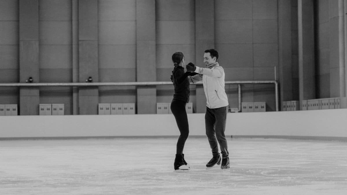 Two adults practicing ice skating routines inside an ice rink.