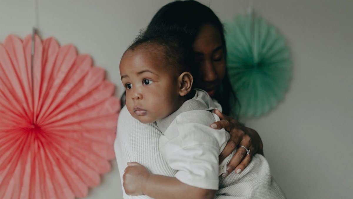 A mother tenderly holding her baby in an indoor setting with colorful decorations adding warmth.