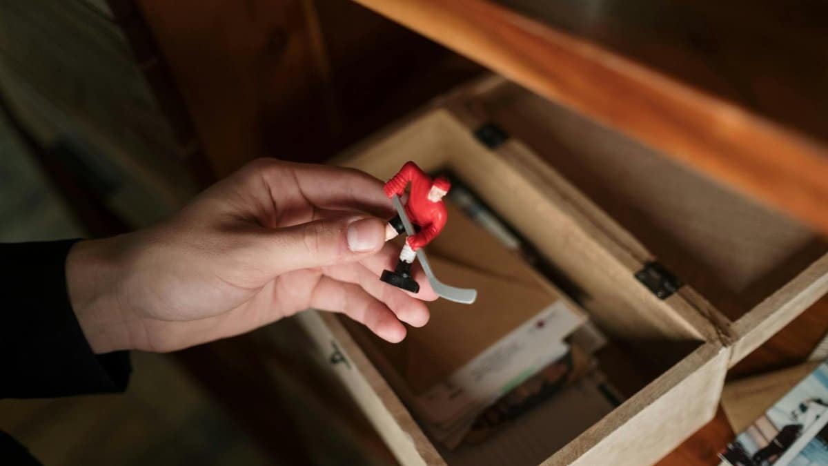 Close-up of a hand holding a vintage hockey toy from a wooden box.