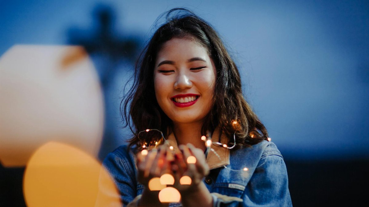 A joyful woman holding string lights, creating a magical ambiance during a nighttime photo shoot.