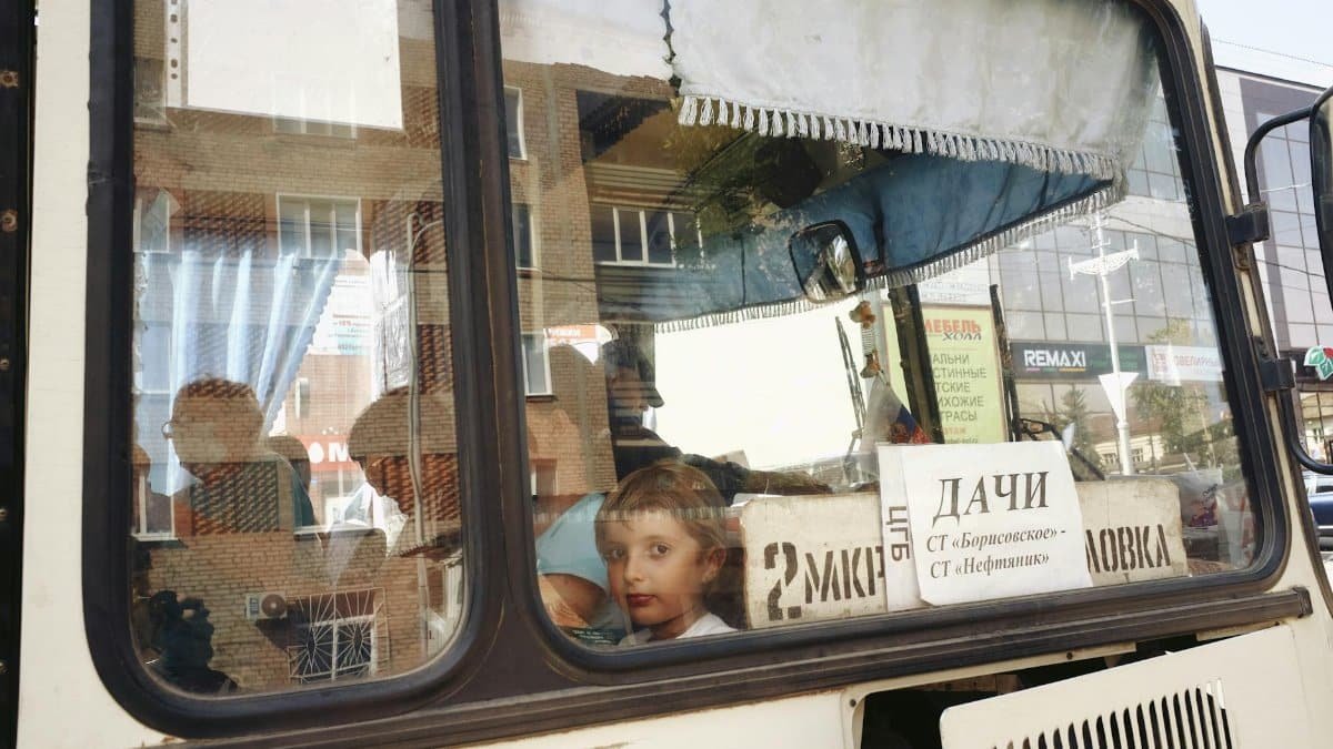 A child looks out the window of a public bus, reflecting urban life.