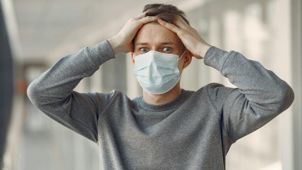 A man indoors wearing a face mask expressing shock and concern, highlighting the importance of health safety.