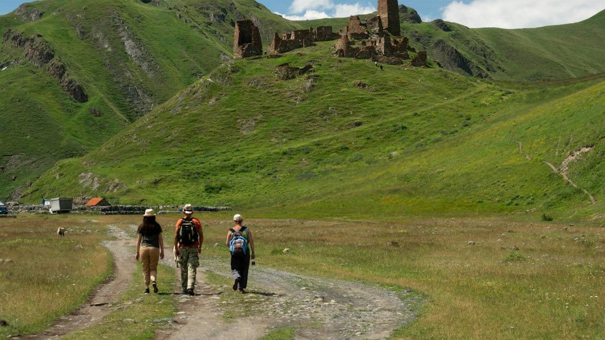 Three hikers walk towards ancient ruins in the scenic mountains of Mtskheta-Mtianeti, Georgia.