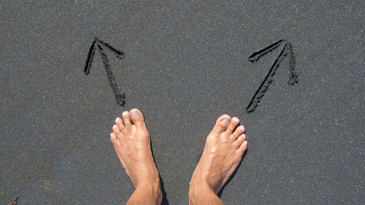 A pair of bare feet on Bali's beach sand with arrows drawn, symbolizing choice and direction.