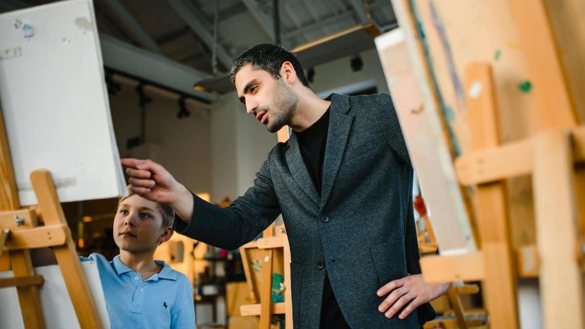 Art teacher instructing a young student in an art studio, focusing on painting techniques.