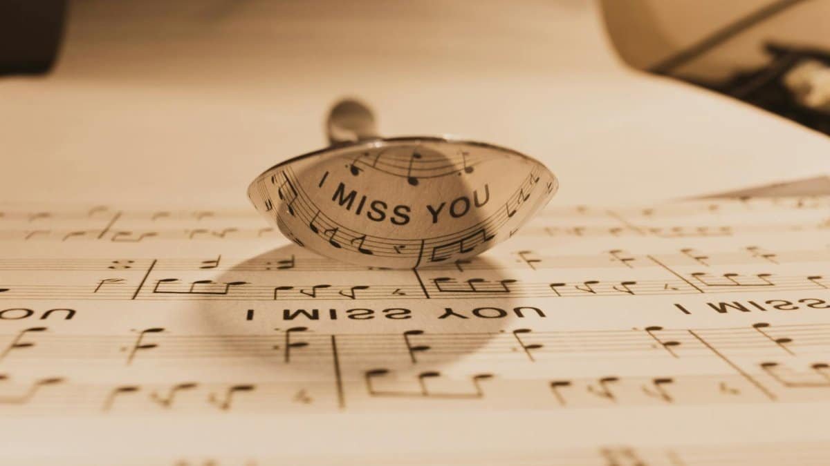 A reflective spoon casting text 'I Miss You' onto sheet music, sepia tone.