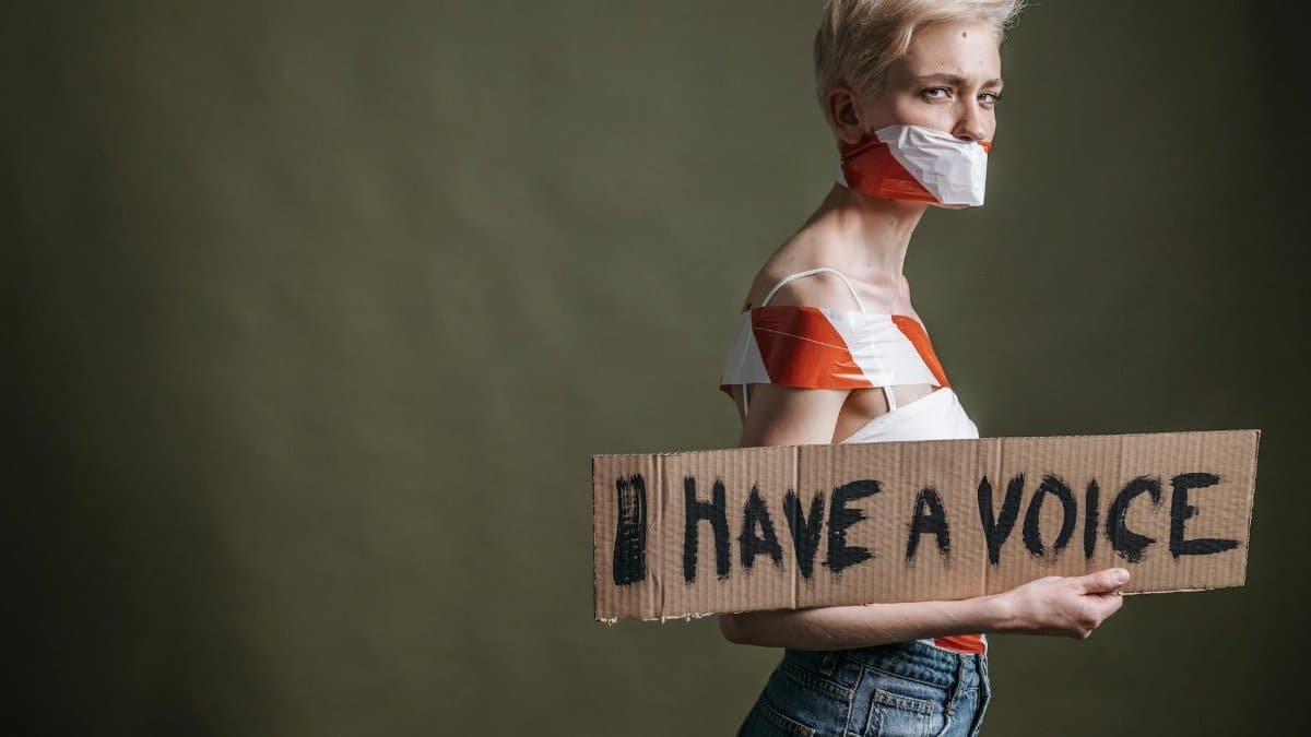 A woman wrapped in tape holds a protest placard saying 'I Have a Voice'.