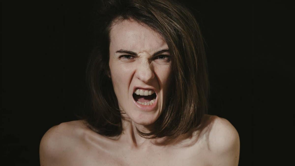 Close-up portrait of a woman expressing intense anger with an open mouth and bare shoulders.