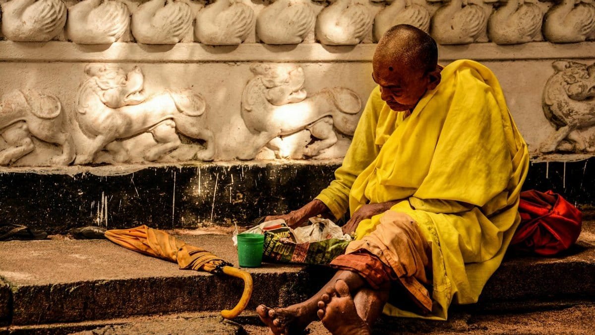 A Buddhist monk in yellow robes meditates on a sidewalk, conveying themes of spirituality and simplicity.