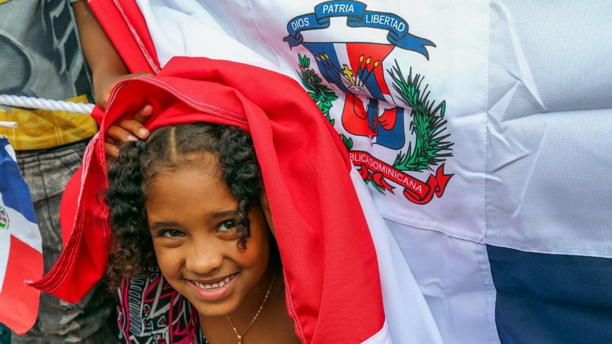 Cheerful young girl smiling beneath a Dominican Republic flag, celebrating national pride.