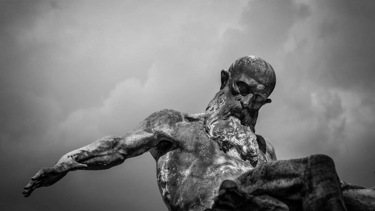 Monochrome photo of a weathered statue under an overcast sky, conveying a dramatic mood.
