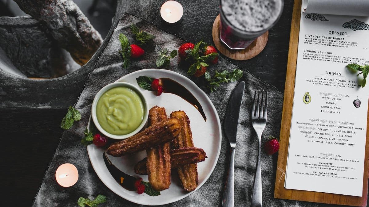 Plate of churros with avocado dip, surrounded by strawberries and candles, perfect for a cozy dining setting.